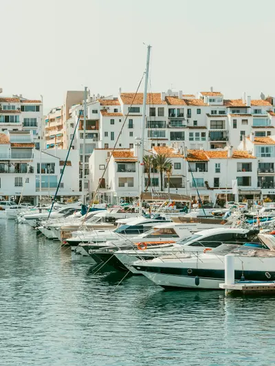 Sailboats and yachts docked in a marina with white buildings.
